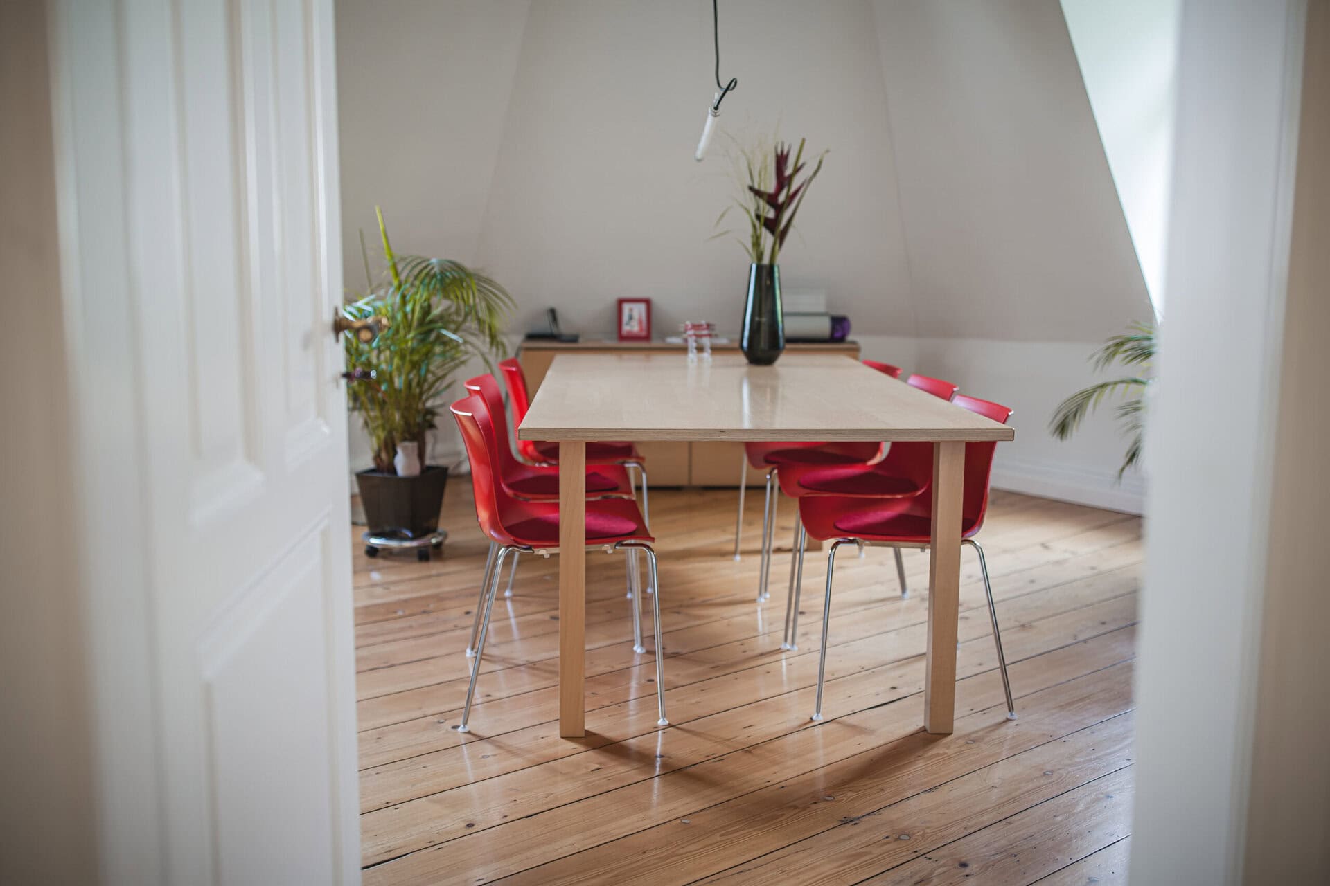 Moderner Besprechungsraum der Kanzlei Räuchle mit roten Stühlen, Holztisch und Pflanzen, ideal für rechtliche Beratung und Mandantengespräche in einer professionellen Umgebung.